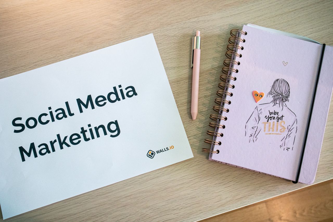 Flat lay of social media marketing paper and motivational notebook on wooden desk.